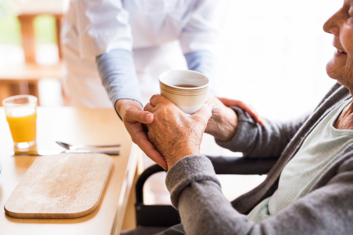 Thuiszorgmedewerker geeft een oudere vrouw in een rolstoel een kopje thee